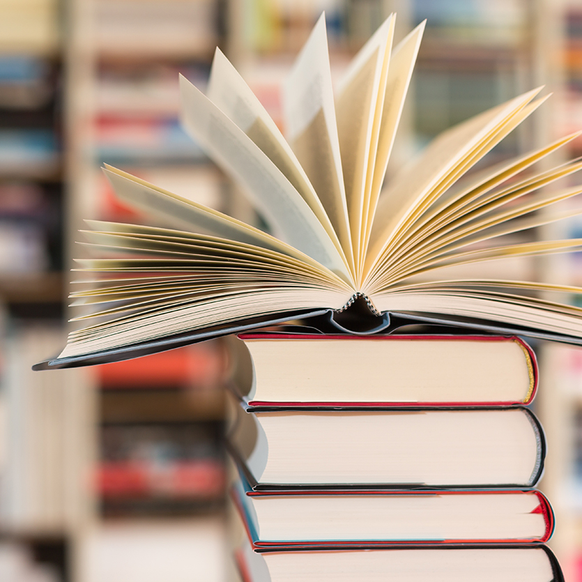 Bücherstapel und oben drauf ein aufgeschlagenes Buch